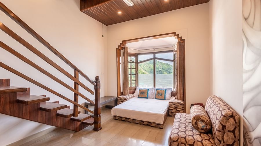 A spacious room near Bhagsunag Temple featuring a wooden staircase, a bed, a sofa, and a large window offering a mountain view – DLS Meghavan Resort.